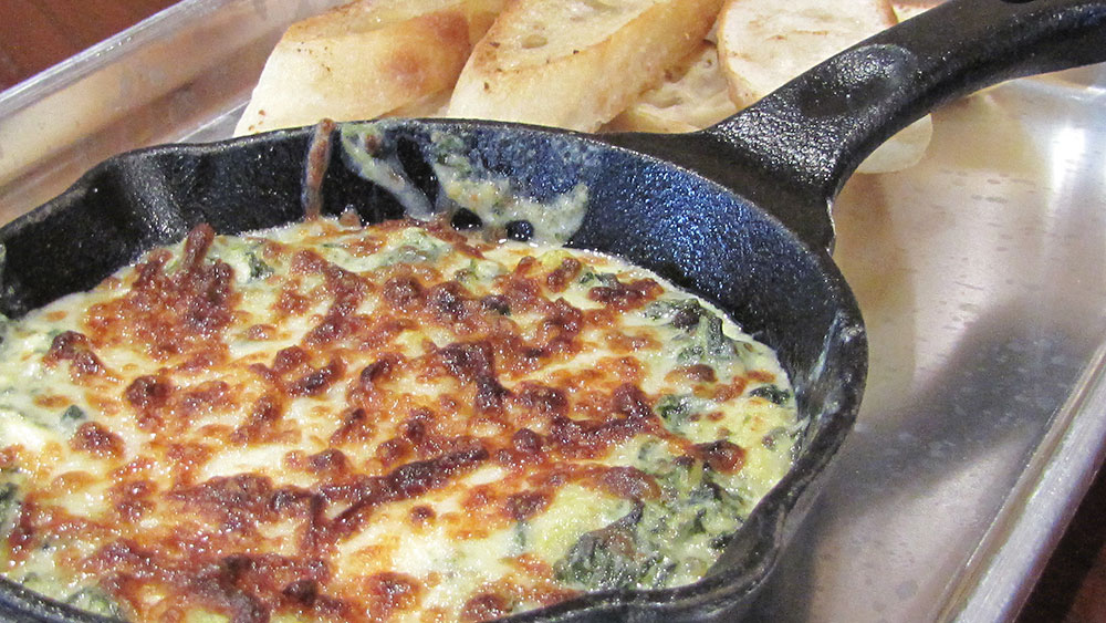 spinach dip in a cast iron pan with bread on the side